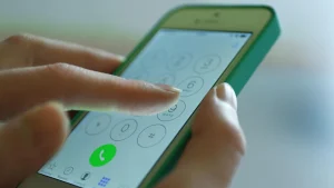 Close-up image of a hand dialing a number on a smartphone's touchscreen—clearly showing the number pad and green call button.
