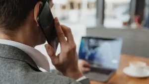 Man in business attire on a phone call while working on a laptop in a café.